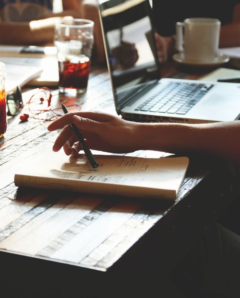 a hand holding a pen above the notebook with project ideas